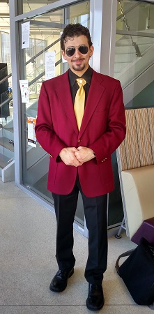 Tony Stark stands in a red blazer, black shirt, and gold tie.