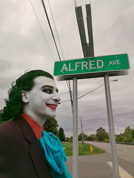 The Joker stands under a street sign for Alfred Avenue.