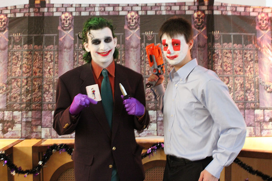 The Joker holds up a Joker card and knife, and a clown henchman holds a blaster and a duffel bag of weapons.