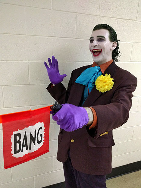 The Joker fires a gun with a flag that says, bang, and laughs.
