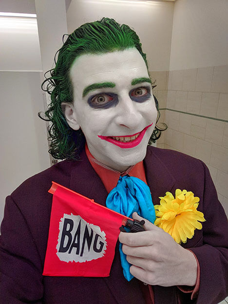 The Joker grins and a gun with a flag that says, bang.