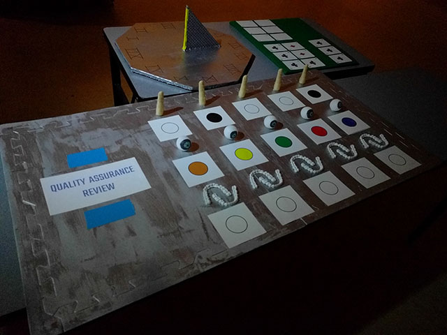 The android parts sit on a silver panel next to a sign labeled, quality assurance review.