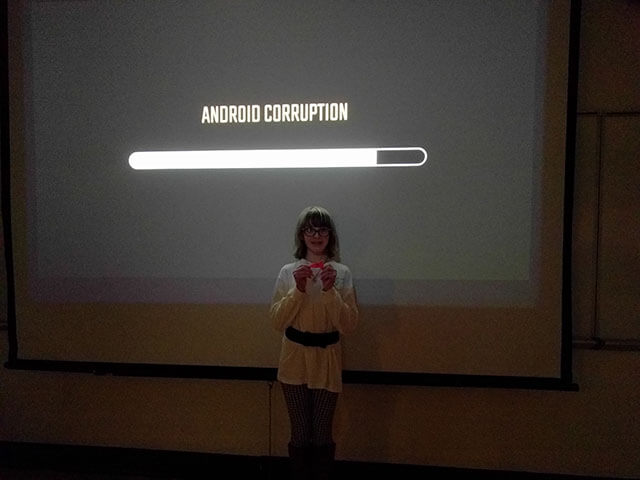 An android stands in front of a wall with a progress bar labeled, Android corruption.